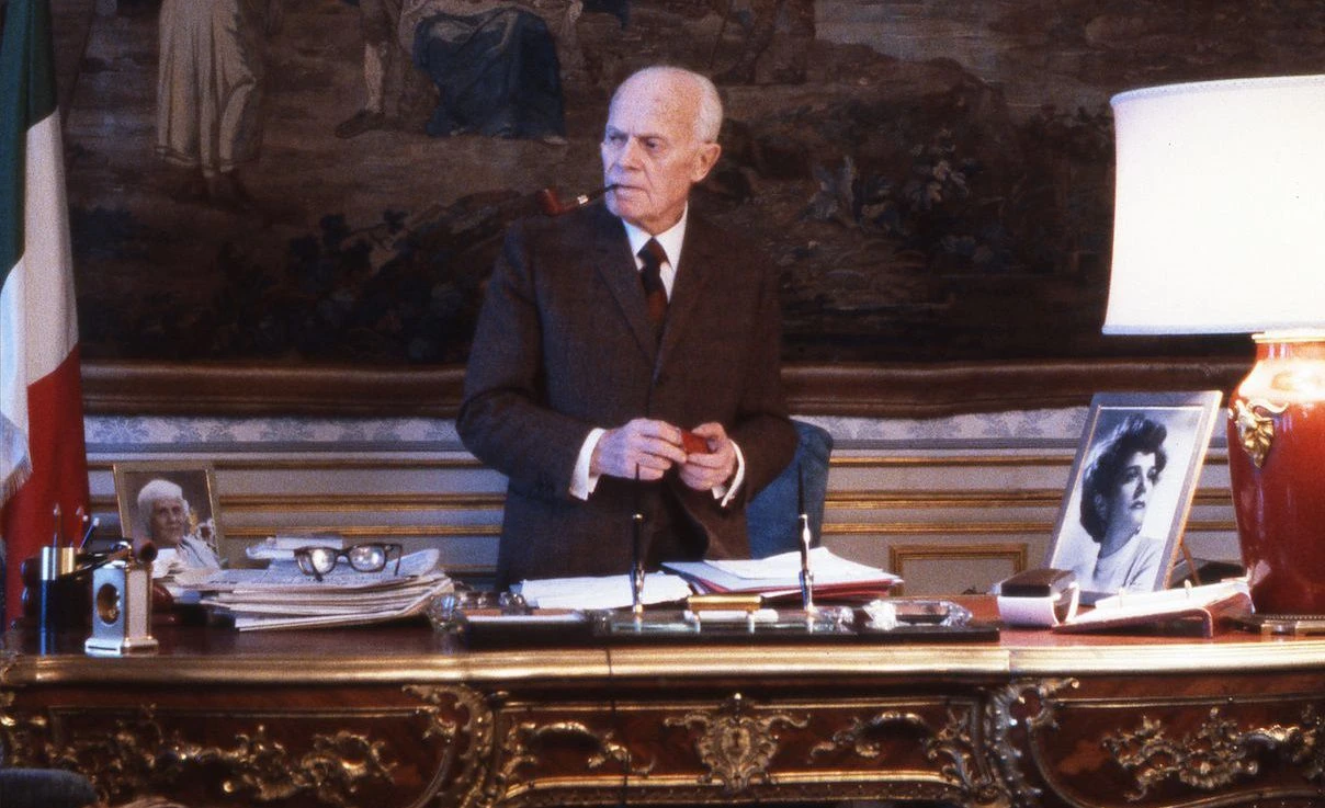 عکس رنگی رئیس جمهور ساندرو پرتینی که پشت میزش ایستاده است.